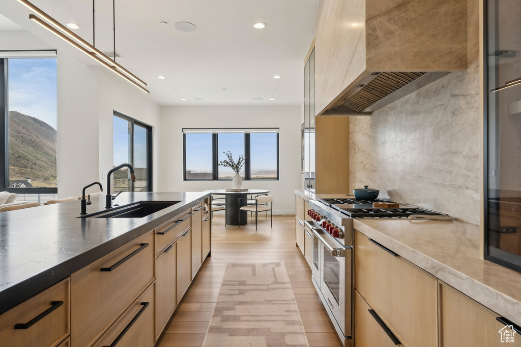 Kitchen featuring light brown cabinetry, a sink, light wood finished floors, stainless steel stove, and wall chimney exhaust hood