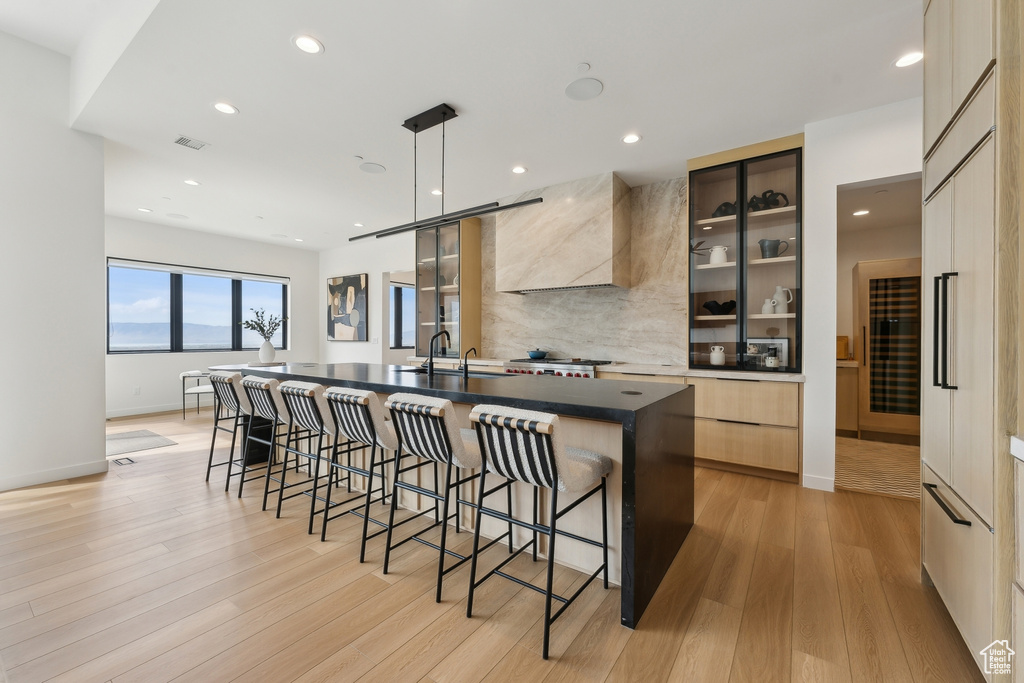 Kitchen featuring wall chimney range hood, light wood finished floors, a breakfast bar area, a spacious island, and modern cabinets