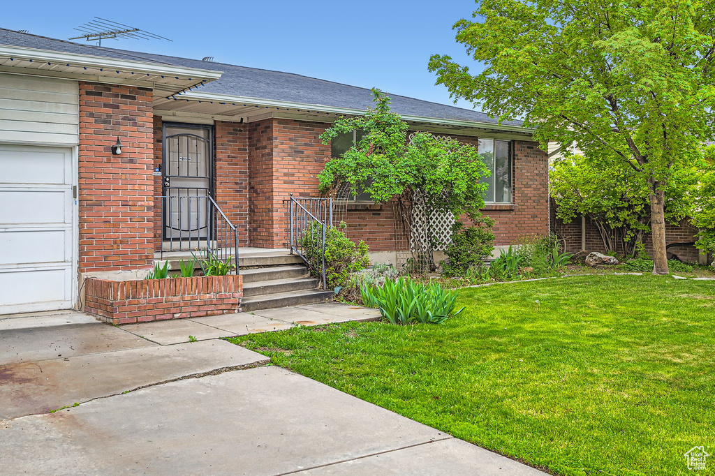 View of front of home with brick siding, a front yard, and a garage