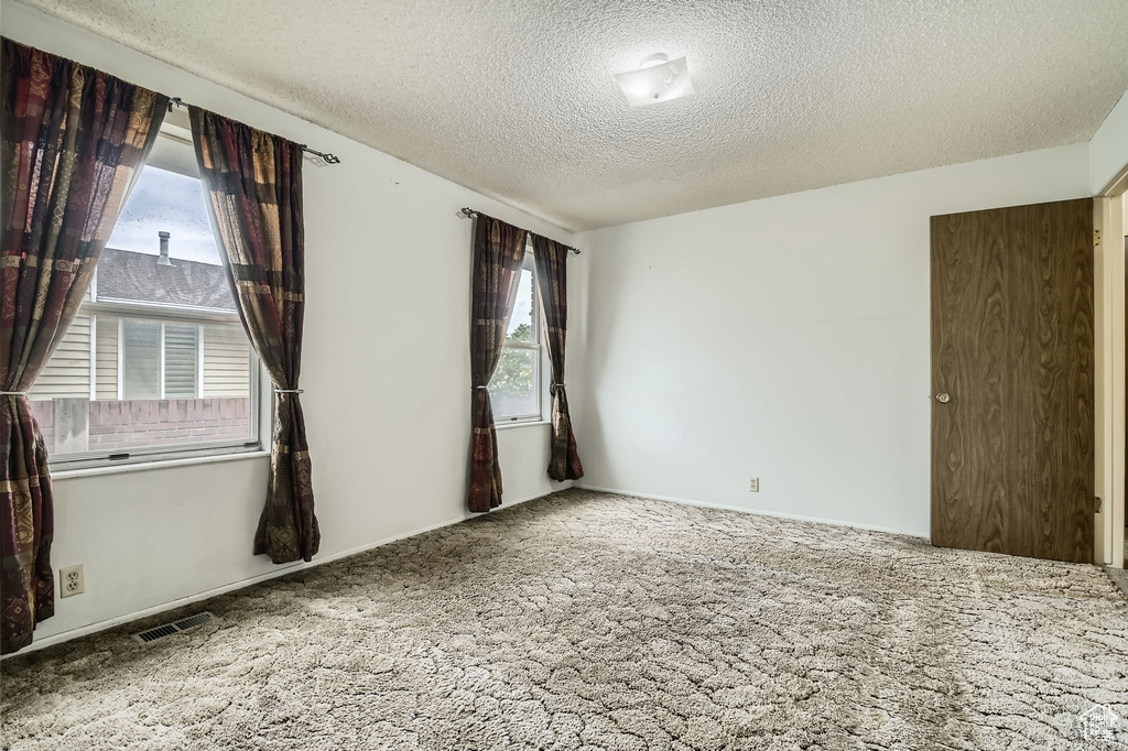 Unfurnished room featuring carpet flooring, a textured ceiling, and visible vents