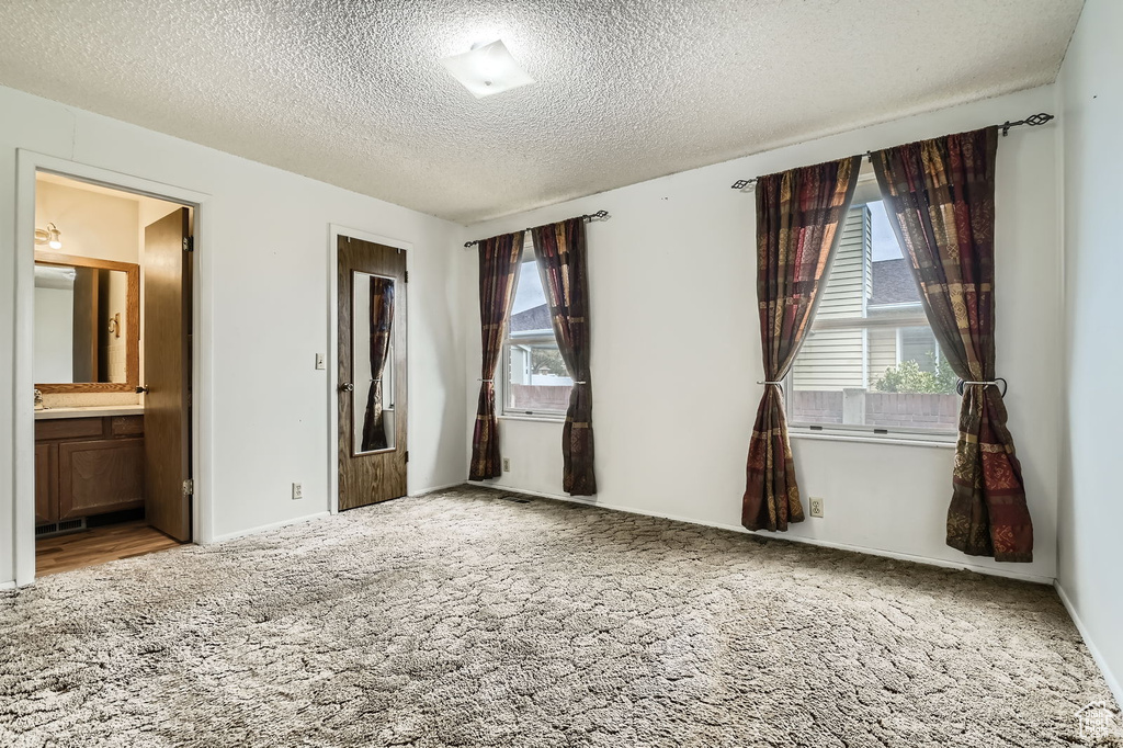 Unfurnished bedroom featuring ensuite bathroom, carpet flooring, and a textured ceiling