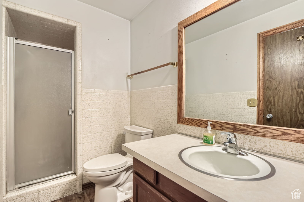 Full bathroom featuring tile walls, wainscoting, a stall shower, vanity, and toilet