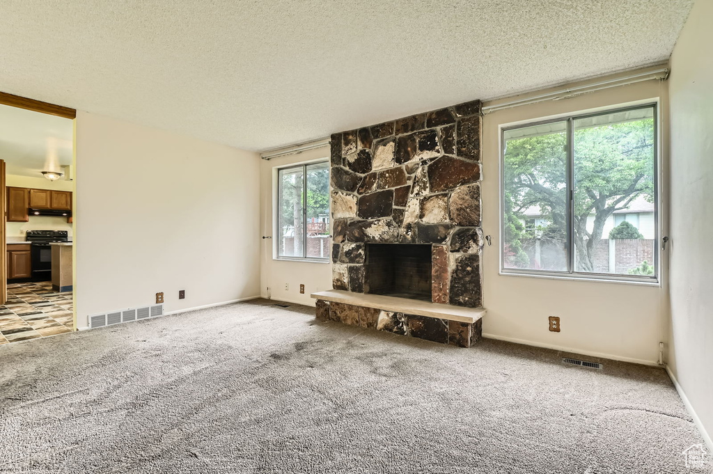 Unfurnished living room with light carpet, a textured ceiling, a stone fireplace, baseboards, and visible vents