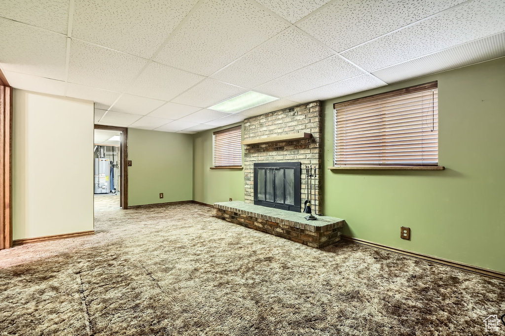 Unfurnished living room featuring a fireplace, baseboards, a paneled ceiling, gas water heater, and carpet flooring