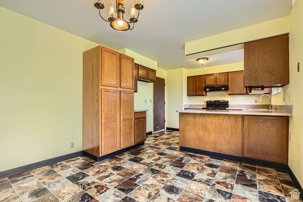 Kitchen featuring stone finish floor, a sink, baseboards, black range oven, and under cabinet range hood