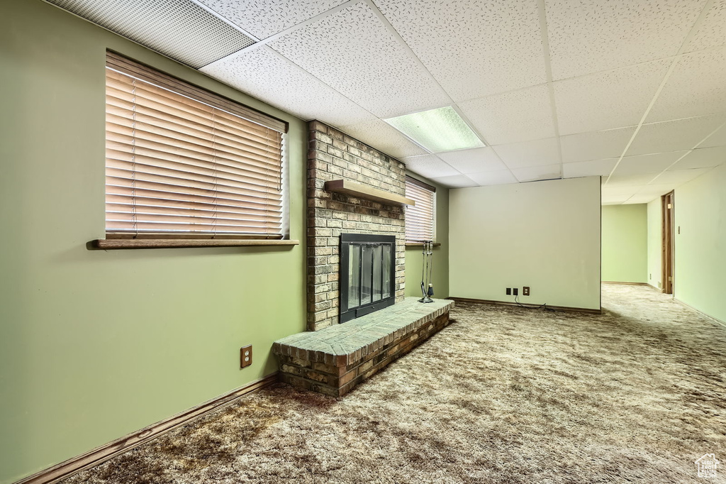 Unfurnished living room with carpet, a paneled ceiling, and a brick fireplace