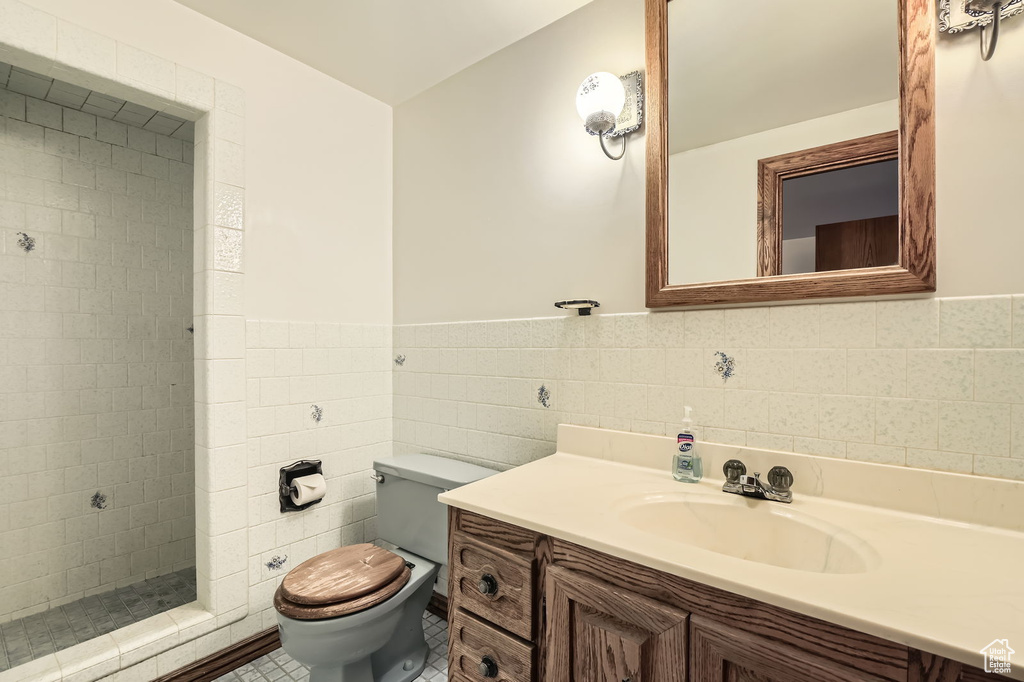 Bathroom featuring tile walls, a tile shower, a wainscoted wall, vanity, and toilet