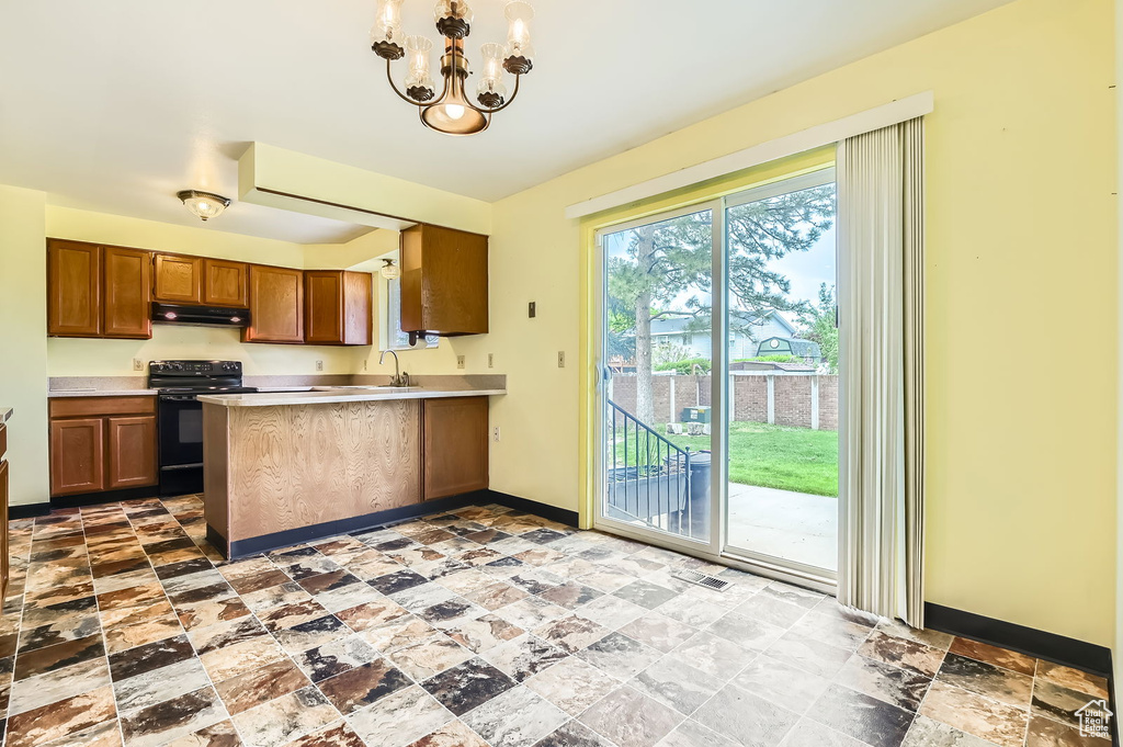 Kitchen with black electric range oven, baseboards, stone finish floor, under cabinet range hood, and brown cabinets
