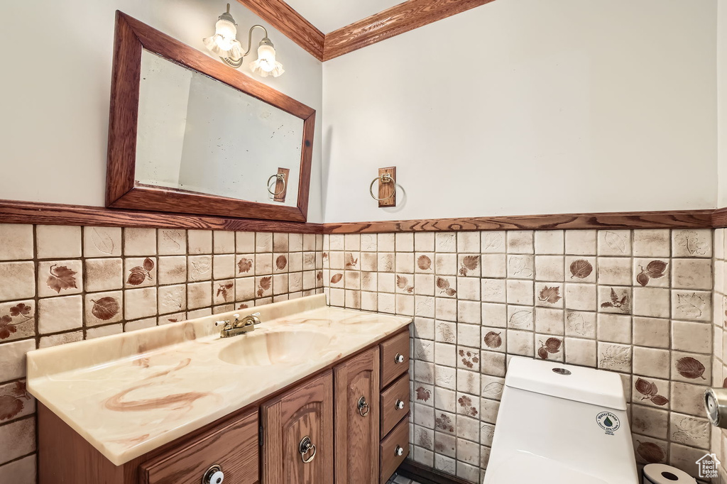 Half bathroom with crown molding, vanity, toilet, and tile walls