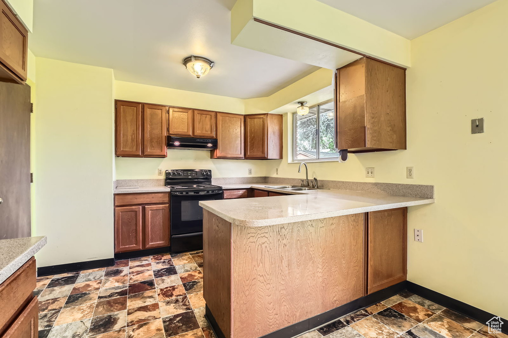 Kitchen featuring a sink, light countertops, black electric range oven, a peninsula, and under cabinet range hood