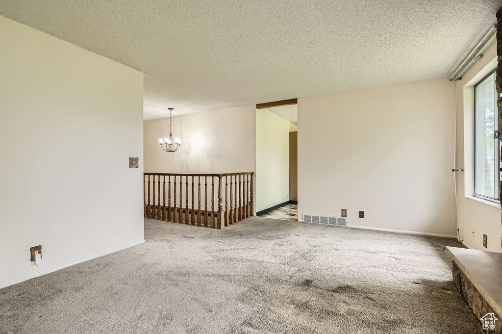 Carpeted empty room featuring a textured ceiling, a chandelier, and visible vents