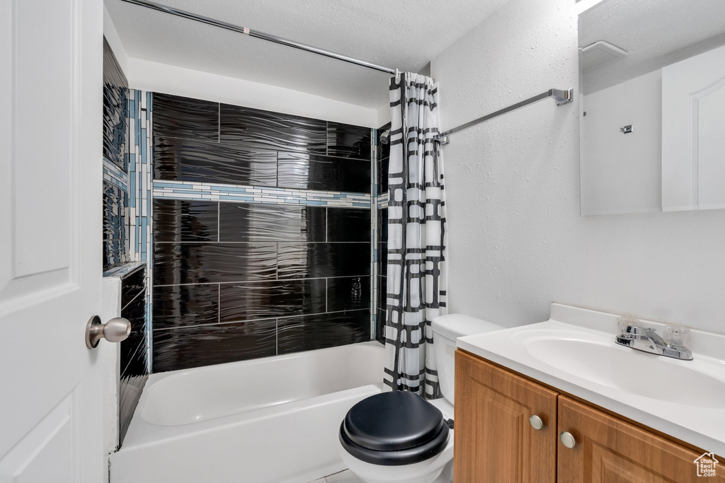 Full bathroom featuring vanity, a textured wall, toilet, and shower / tub combo