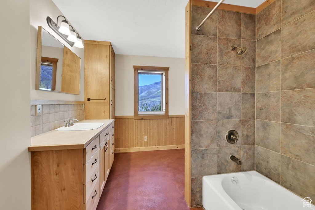 Bathroom featuring concrete flooring, wood walls, shower / tub combination, vanity, and a wainscoted wall