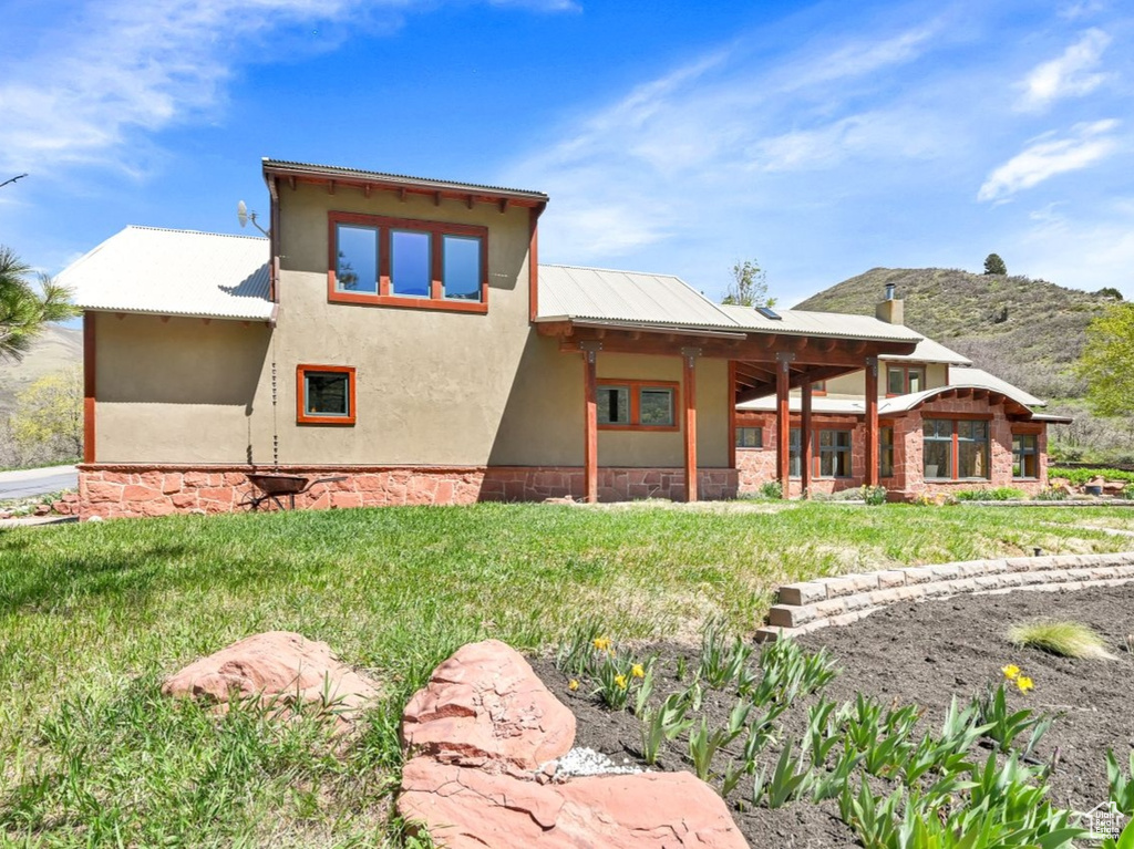 Rear view of property featuring a lawn, a mountain view, stucco siding, and stone siding