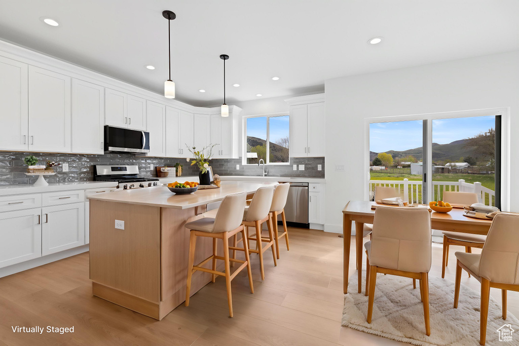 Kitchen with stainless steel appliances, backsplash, light wood-style flooring, a center island, and recessed lighting