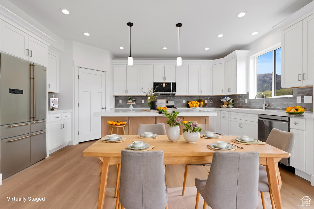 Kitchen featuring appliances with stainless steel finishes, a sink, light countertops, white cabinets, and backsplash