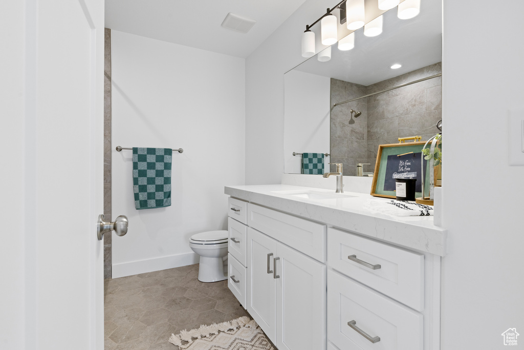 Bathroom featuring visible vents, a tile shower, vanity, baseboards, and toilet