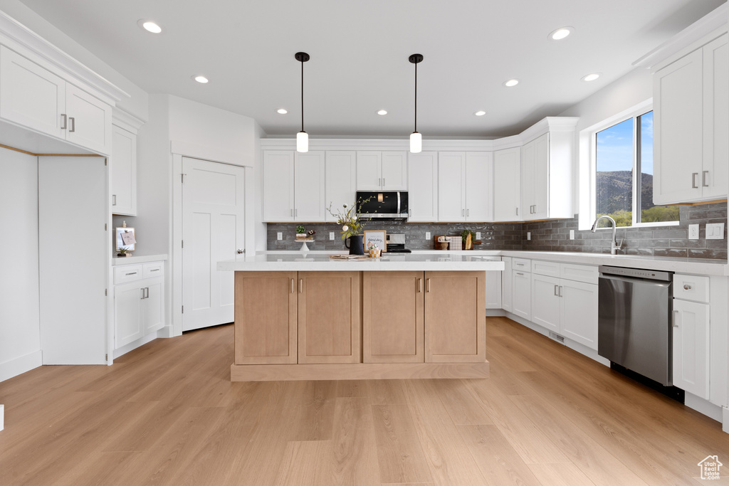 Kitchen with a kitchen island, white cabinets, light wood-style flooring, appliances with stainless steel finishes, and backsplash