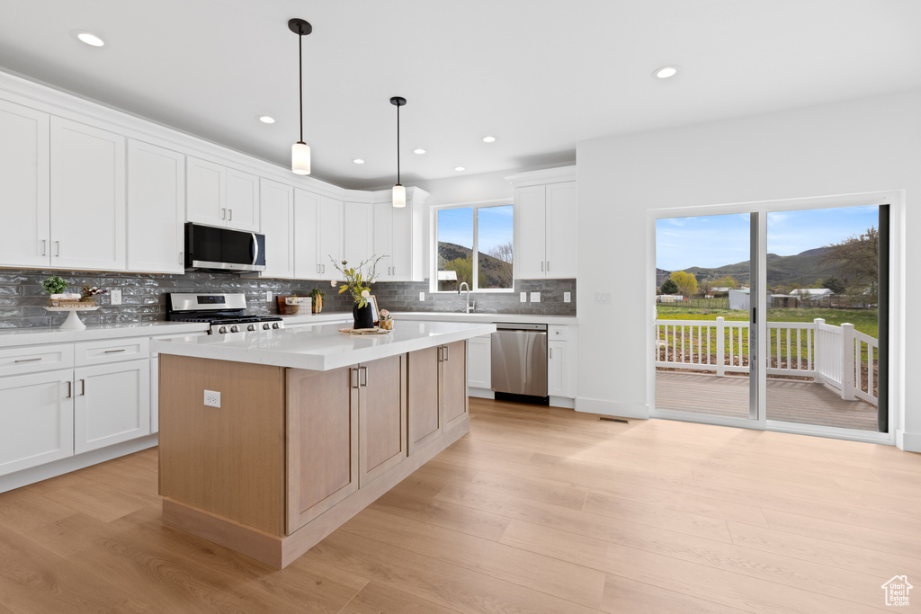 Kitchen featuring decorative backsplash, appliances with stainless steel finishes, a center island, light countertops, and light wood finished floors
