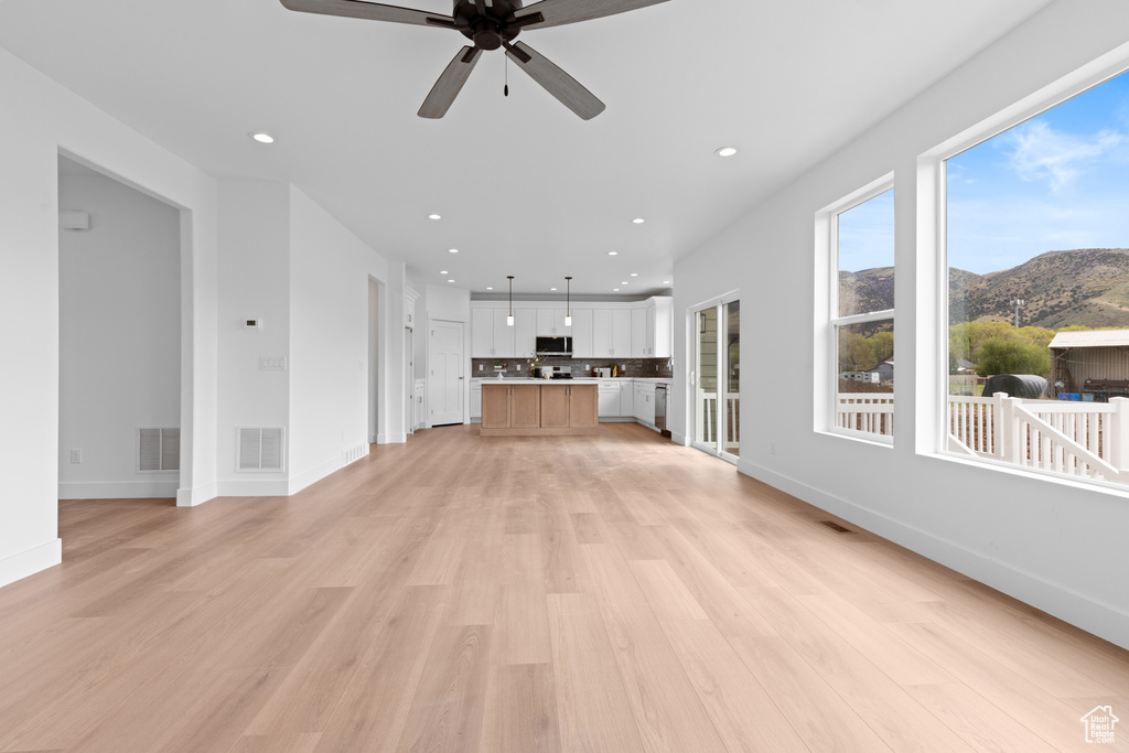 Unfurnished living room with light wood-style floors, a ceiling fan, a mountain view, and visible vents