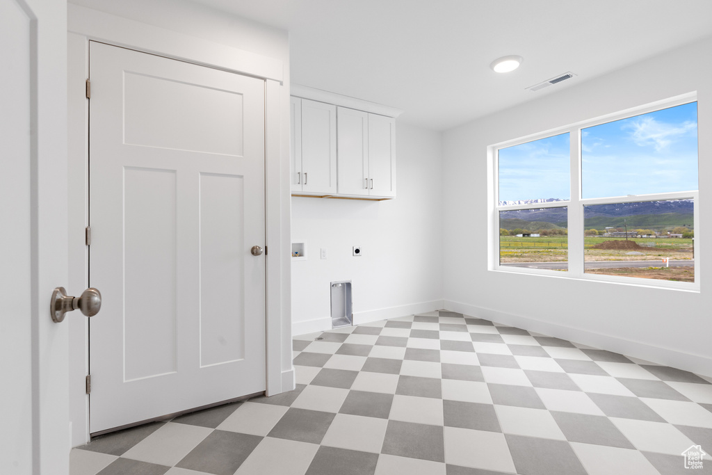 Laundry area with hookup for an electric dryer, visible vents, cabinet space, baseboards, and light floors