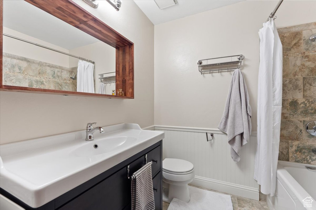 Full bathroom with a wainscoted wall, shower / bathtub combination with curtain, vanity, and toilet