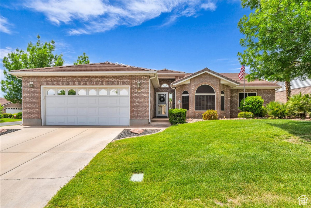 Single story home featuring an attached garage, a tile roof, a front lawn, brick siding, and concrete driveway