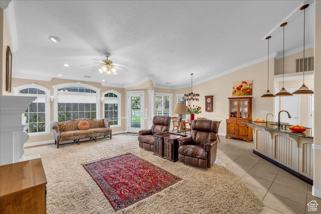 Living area featuring light tile patterned flooring, baseboards, ornamental molding, and ceiling fan with notable chandelier