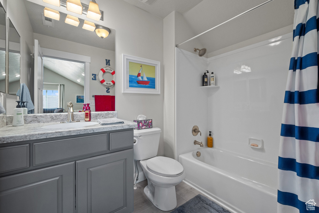 Bathroom featuring vaulted ceiling, wood finished floors, shower / tub combo, vanity, and toilet