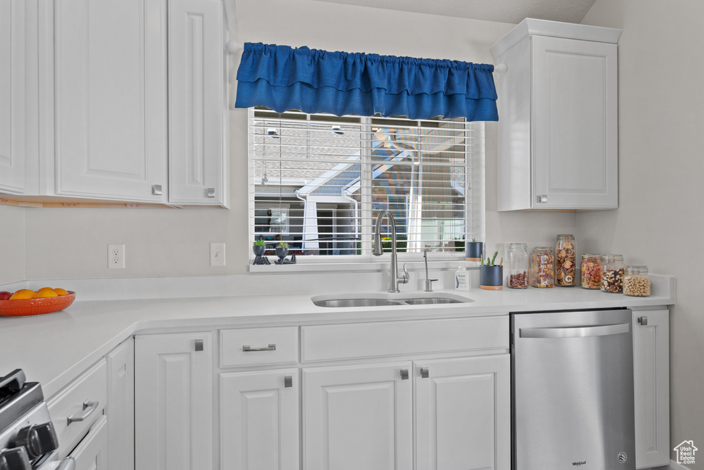 Kitchen featuring stainless steel dishwasher, white cabinetry, a sink, and light countertops