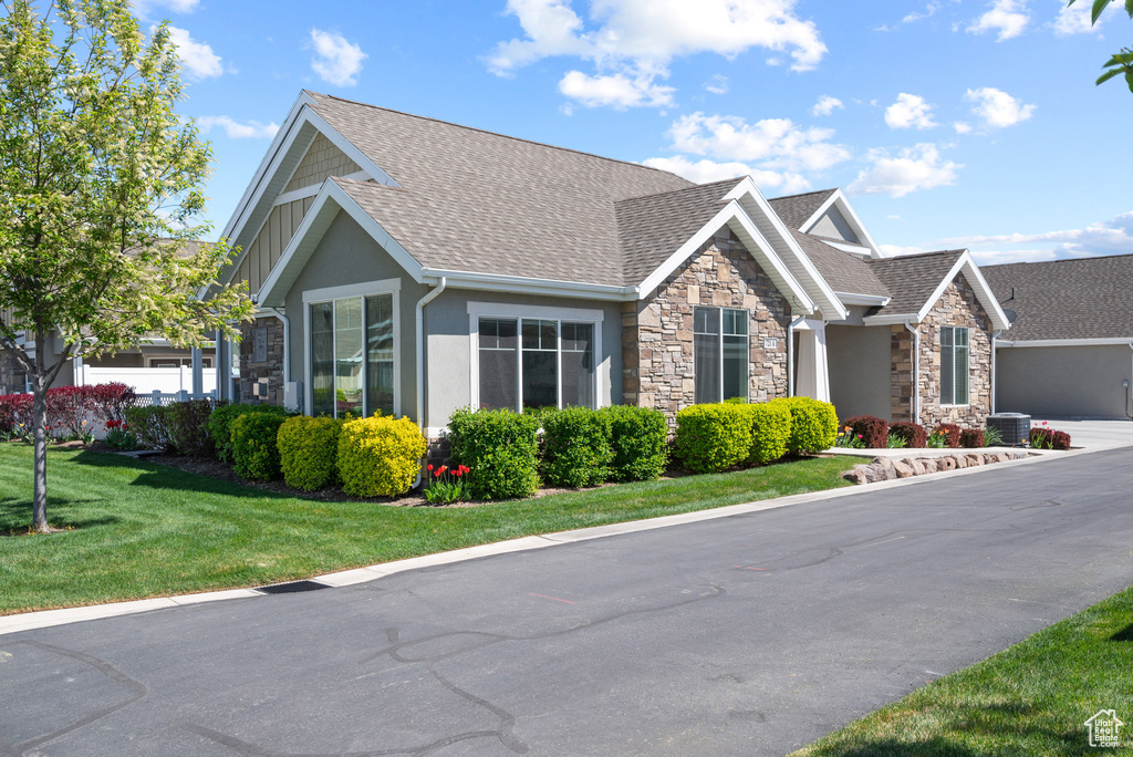 View of front facade featuring a shingled roof, stucco siding, a front yard, and stone siding