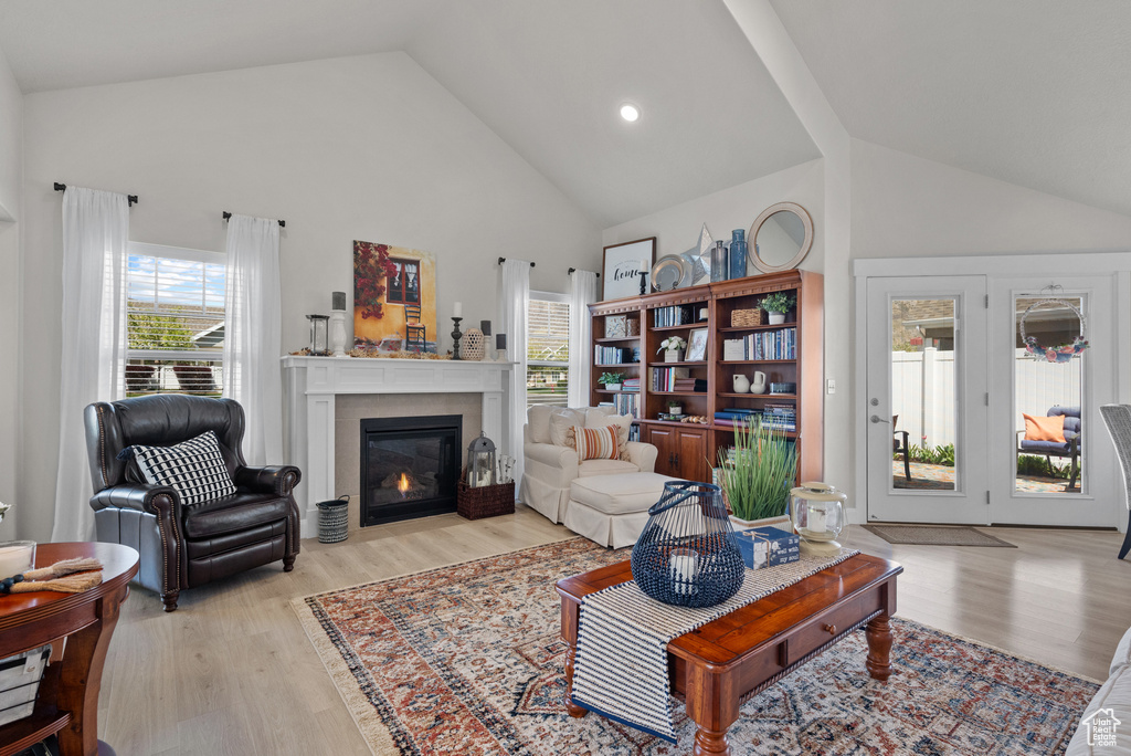 Living area with light wood-style floors, a glass covered fireplace, and high vaulted ceiling