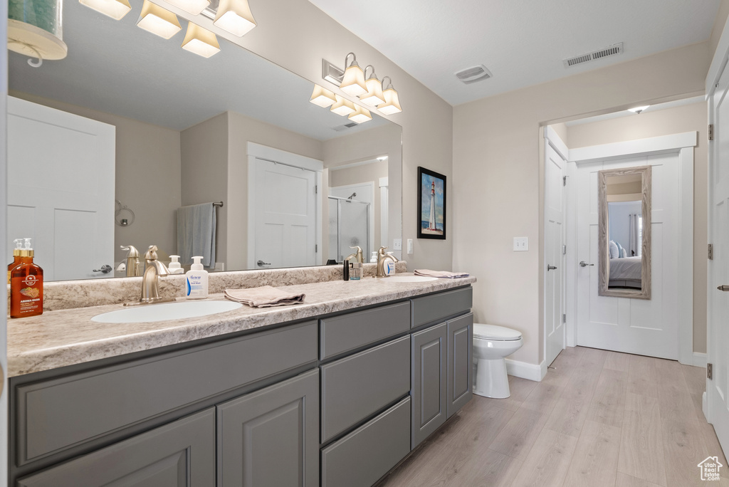 Full bath featuring visible vents, double vanity, wood finished floors, toilet, and a sink