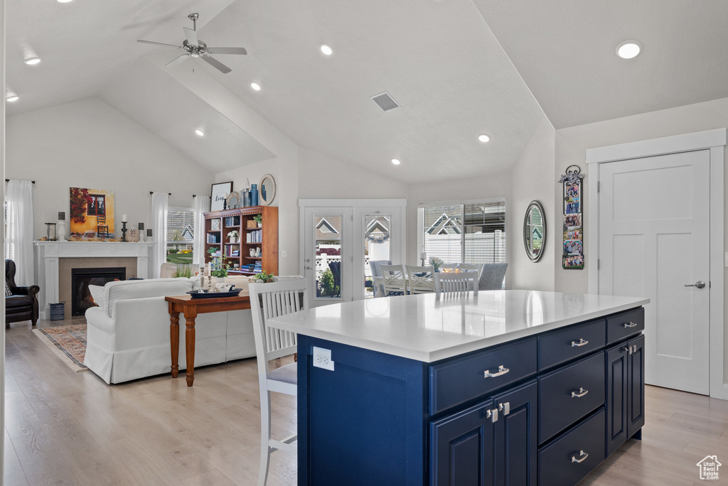 Kitchen with a ceiling fan, blue cabinetry, a fireplace, light countertops, and light wood finished floors