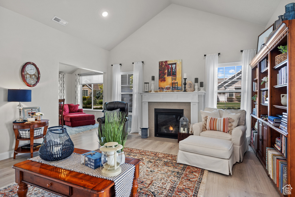 Living room with visible vents, a fireplace with flush hearth, light wood-style flooring, and high vaulted ceiling