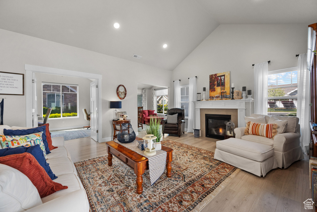 Living room with visible vents, a fireplace with flush hearth, wood finished floors, high vaulted ceiling, and recessed lighting