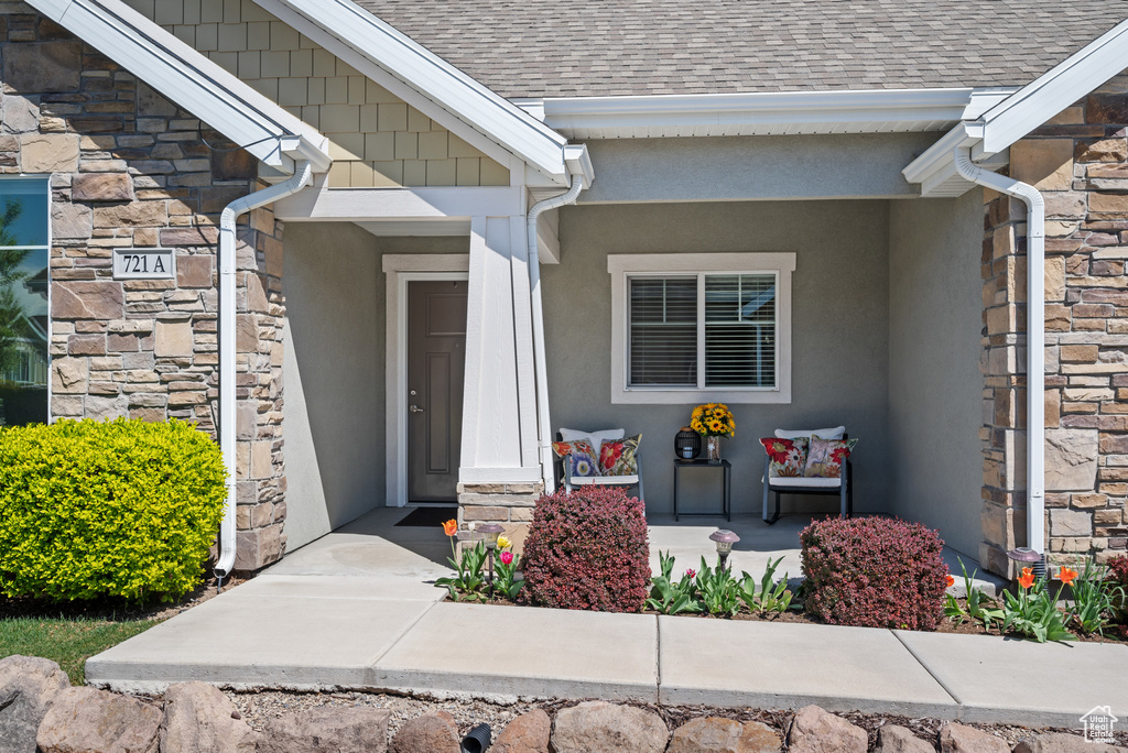 Entrance to property featuring a shingled roof, stucco siding, and stone siding