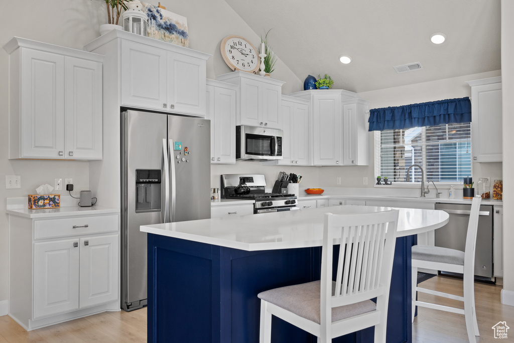 Kitchen with visible vents, a kitchen bar, white cabinets, appliances with stainless steel finishes, and vaulted ceiling