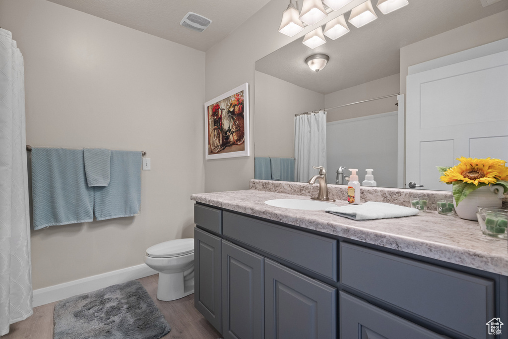 Full bathroom featuring vanity, toilet, baseboards, wood finished floors, and visible vents