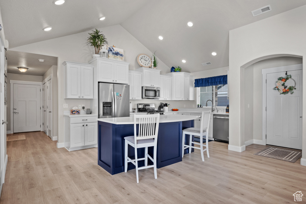 Kitchen featuring white cabinets, high vaulted ceiling, appliances with stainless steel finishes, and a breakfast bar
