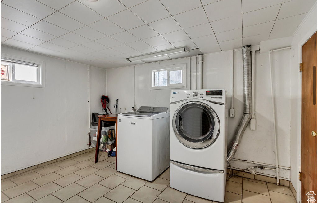 Clothes washing area featuring a healthy amount of sunlight, laundry area, light tile patterned flooring, and washing machine and clothes dryer