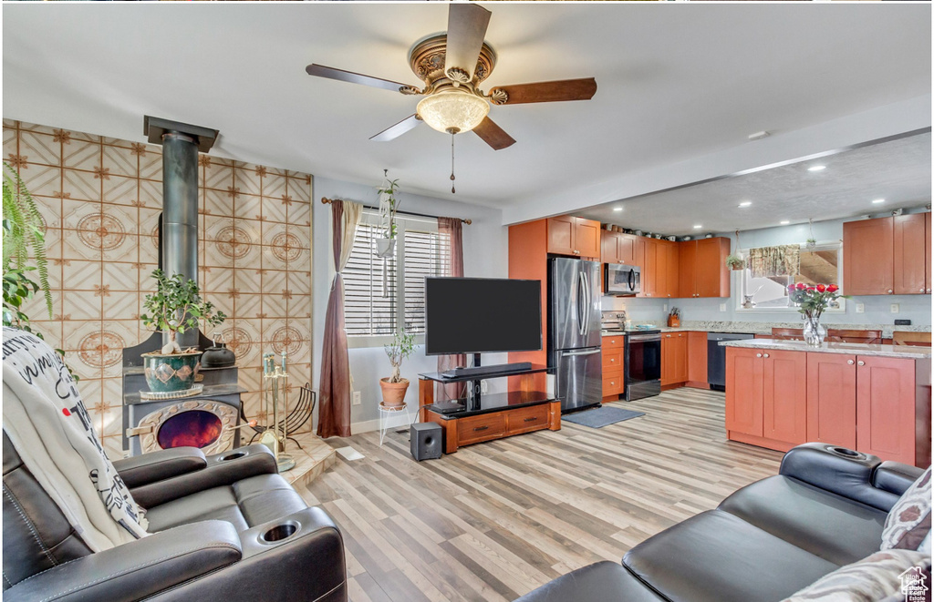 Living room with ceiling fan, a wood stove, baseboards, recessed lighting, and light wood-style flooring