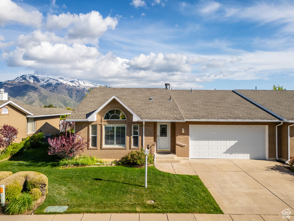 Single story home featuring roof with shingles, an attached garage, brick siding, a front yard, and driveway