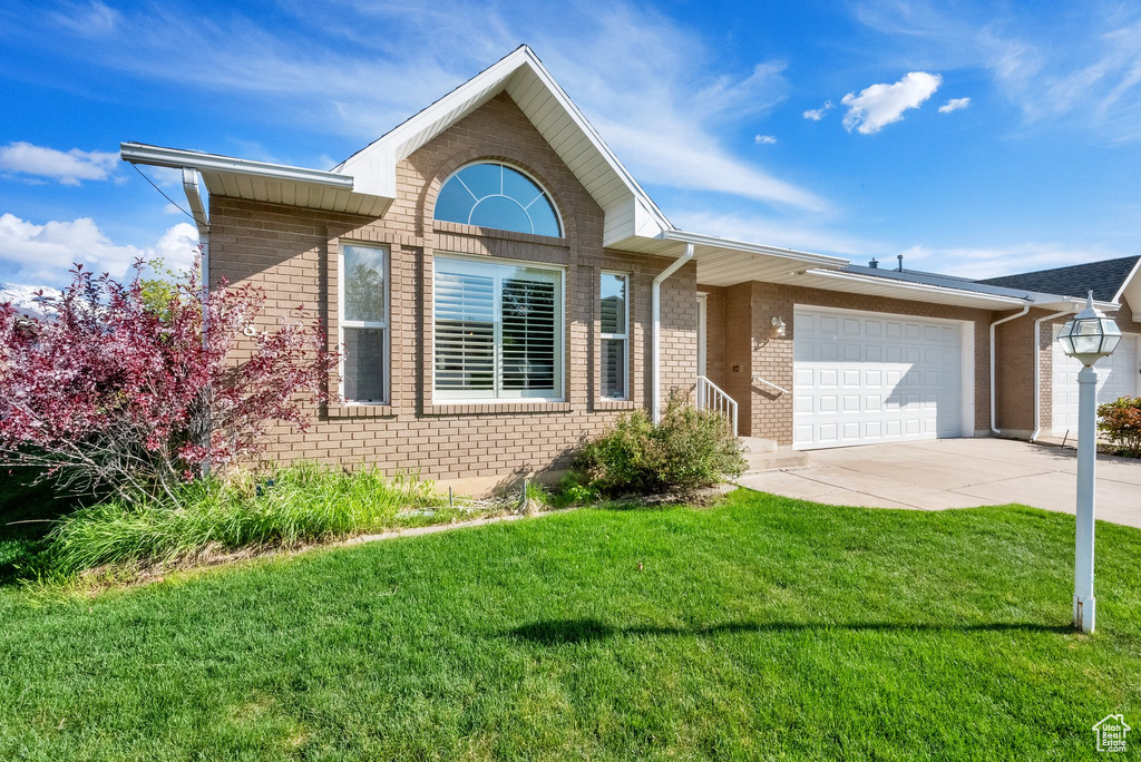 Ranch-style home with an attached garage, driveway, a front lawn, and brick siding
