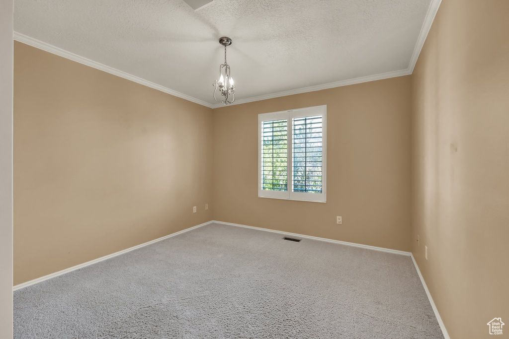 Carpeted empty room featuring baseboards, ornamental molding, a notable chandelier, and visible vents