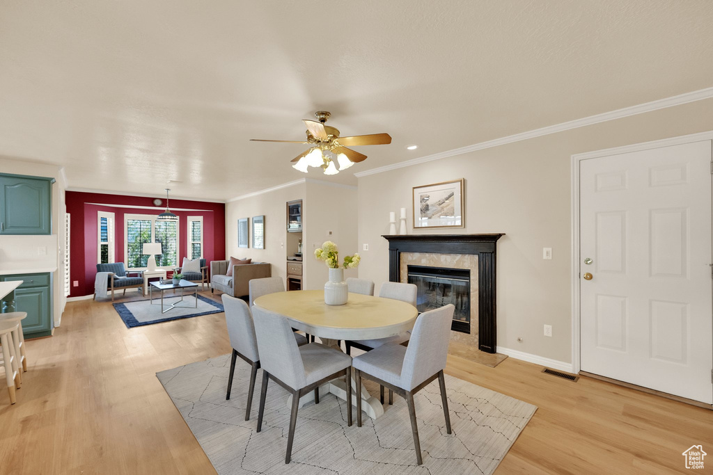 Dining area featuring a premium fireplace, a ceiling fan, ornamental molding, and light wood-type flooring