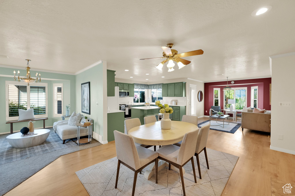 Dining space with crown molding, light wood-style floors, baseboards, recessed lighting, and ceiling fan with notable chandelier