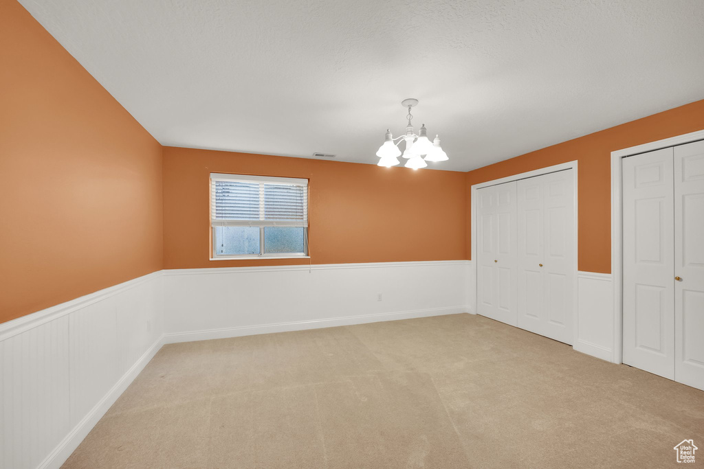 Empty room featuring an inviting chandelier, visible vents, wainscoting, and light colored carpet