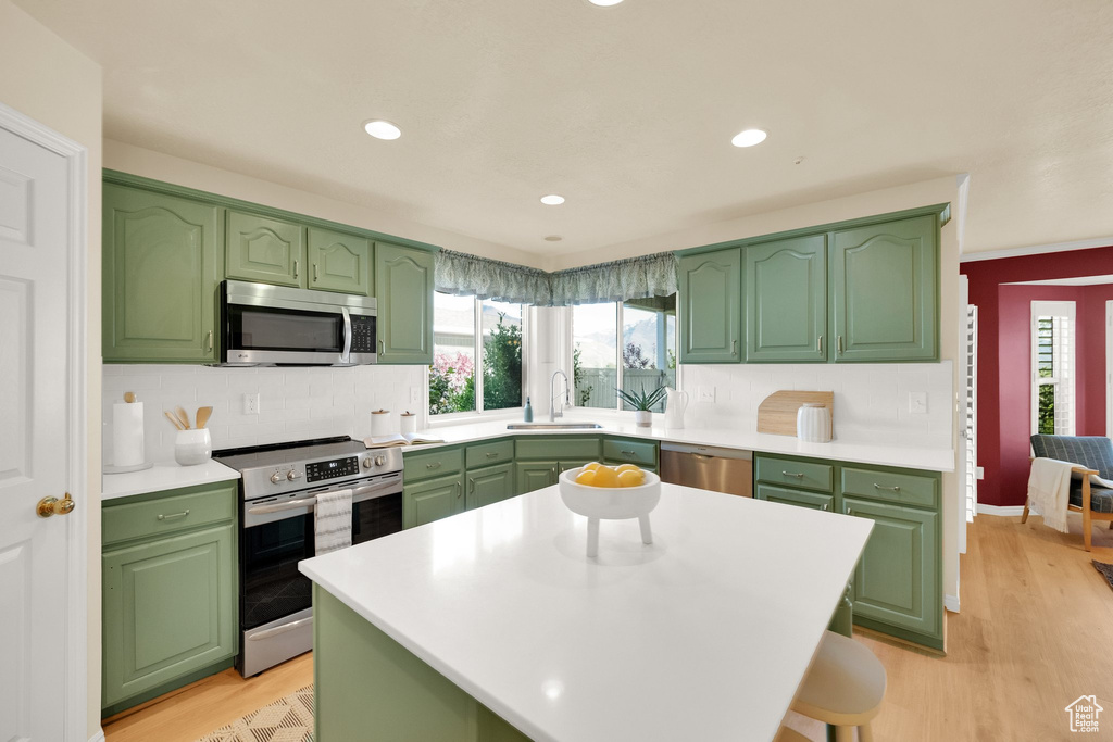 Kitchen with appliances with stainless steel finishes, a sink, light wood-style flooring, tasteful backsplash, and green cabinets