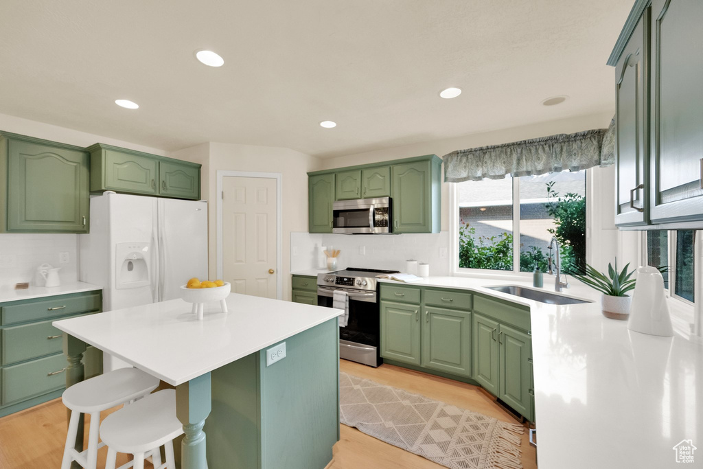 Kitchen featuring a kitchen bar, appliances with stainless steel finishes, a sink, light countertops, and green cabinetry